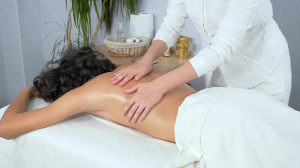 masseuse gives medical massage to young curly haired guy in spa