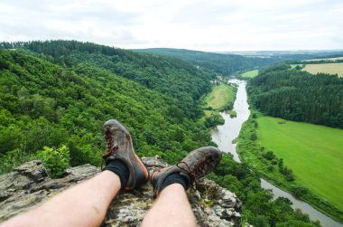 Bacaklar yüksek dağın tepesinde oturan ve nehir manzaraya bakarak gezgin. Doğal Özgürlük kavramı