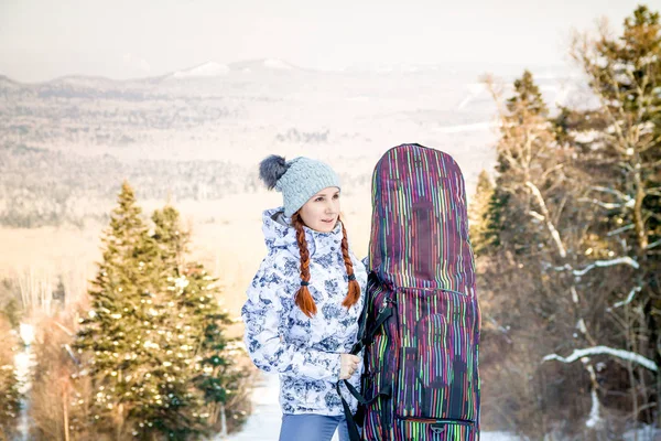 Flicka snowboardåkare stående på ett skidspår, hålla ett fall med hennes snowboard och njuter av skidorten Stockbild