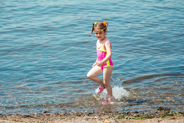 Liten flicka i en baddräkt bada i havet på sommaren, gör ett stänk och kör i vatten Royaltyfria Stockfoton