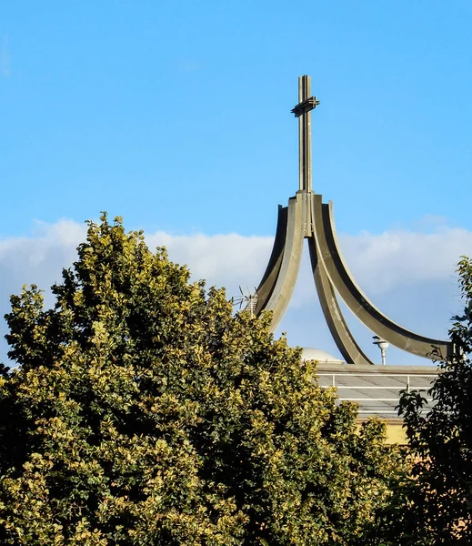 A modern steel church spire rises above the trees in Ostia