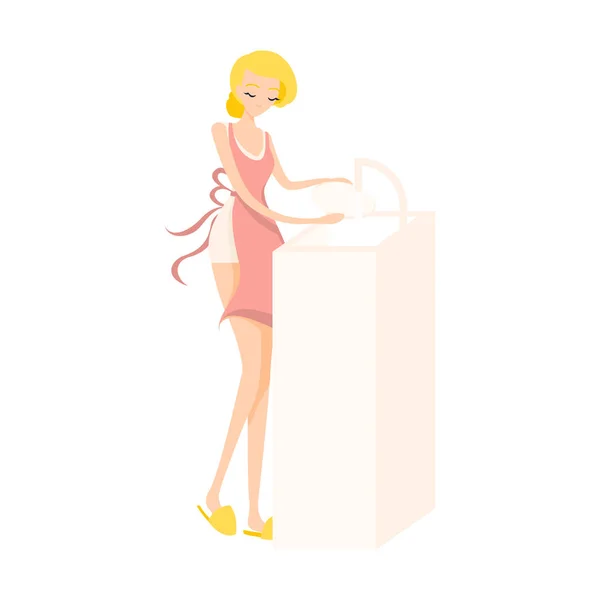 Menina loira bonito está lavando pratos em um avental rosa . —  Vetores de Stock