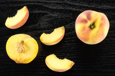 Bir sarı şeftali, bir bölümü yarım ve üç dilimleri, flatlay, siyah ahşap adam üzerinde