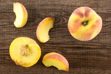 Bir sarı şeftali, bir bölümü yarım ve üç dilimleri, flatlay, kahverengi ahşap adam üzerinde