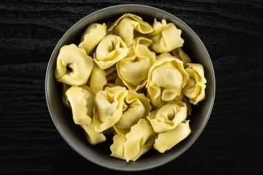 Siyah ahşap arka plan İtalyan geleneksel dumplin üzerinde gri Seramik kase flatlay ham tortellini makarna