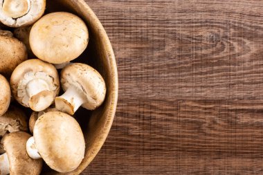 Fresh brown champignons in a wooden bowl top view on brown wood background raw mushroom clipart