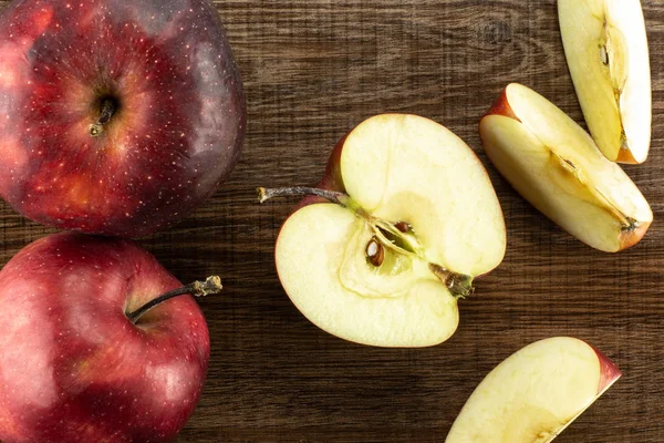 Kırmızı lezzetli elma flatlay kahverengi ahşap zemin iki bütün yarım ve üç dilim üzerinde dilimlenmiş