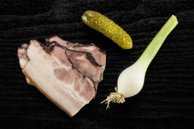 Üç dilim İngilizce pastırma ile tuzlu salatalık ve taze soğan flatlay siyah ahşap üzerine Grup