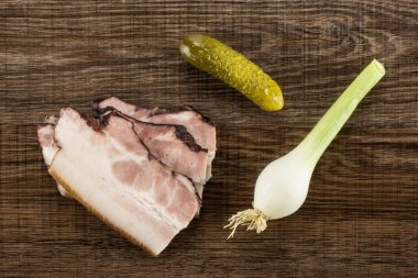 Üç dilim İngilizce pastırma ile bir tuzlu salatalık ve taze soğan flatlay kahverengi ahşap üzerine Grup