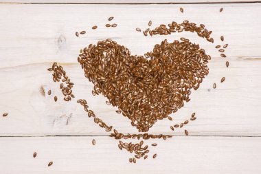 Bütün taze kahverengi flaxseeds kalp flatlay beyaz tahta üzerinde çok