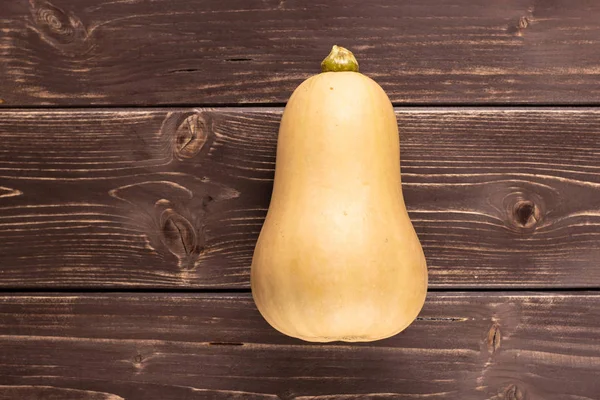 One whole smooth pear shaped orange butternut squash waltham variety flatlay on brown wood