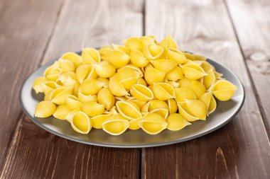 Tüm çiğ sarı makarna conchiglie çeşitli kahverengi ahşap üzerine gri Seramik plaka üzerinde çok