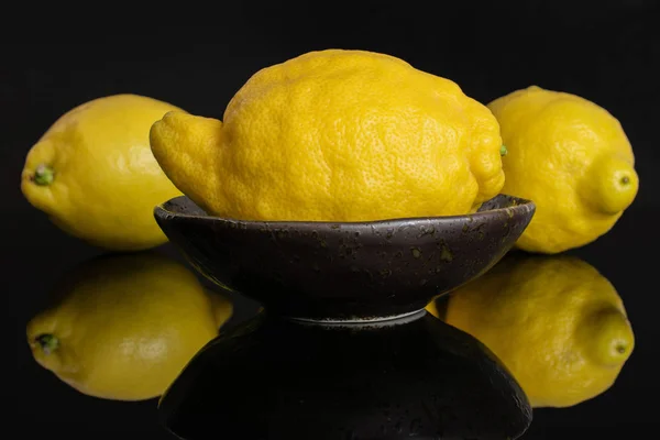 Fresh yellow lemon isolated on black glass