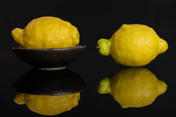 Fresh yellow lemon isolated on black glass