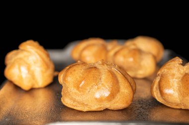 Altın fırınlanmış profiterol siyah camda izole edilmiş.