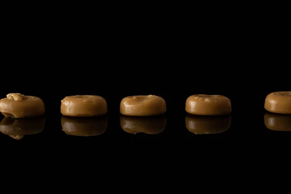 Коричневі карамельні цукерки ізольовані на чорному склі. — стокове фото