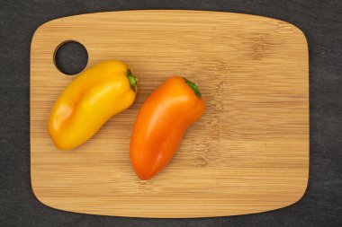 Bambu üzerine iki taze biber grubu. Gri taşın üzerinde tahta kesme tahtası.