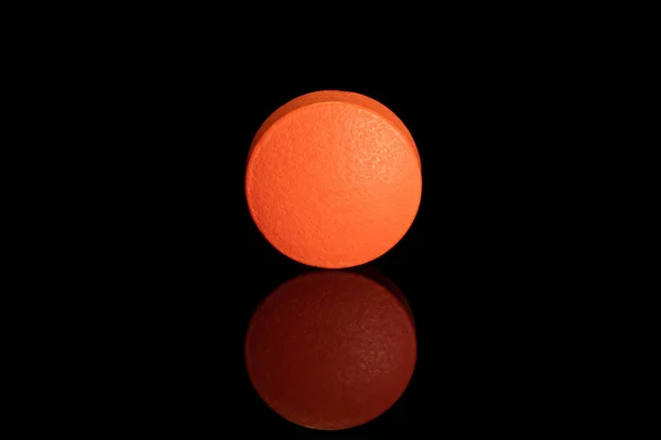 Pomarańczowa tabletka farmaceutyczna izolowana na czarnym szkle — Zdjęcie stockowe