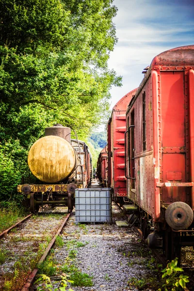 Vários vagões enferrujados e trem nas trilhas — Fotografia de Stock