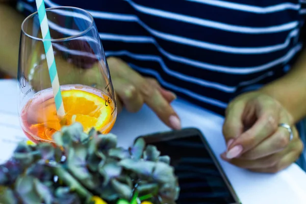 bir kadın aperol bir bardak içerken bir cep telefonu yazıyor 