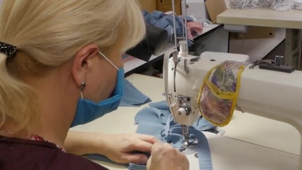 Las trabajadoras de una fábrica de prendas de vestir con máscaras médicas en la cara cosen máscaras protectoras durante la pandemia del virus COVID-19. Lucha contra la pandemia de COVID-19 . — Vídeos de Stock