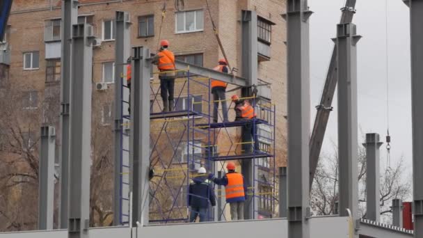 Un groupe de travailleurs masculins en vestes jaunes et chapeaux durs travaillent à une hauteur avec des poutres de fer . — Video