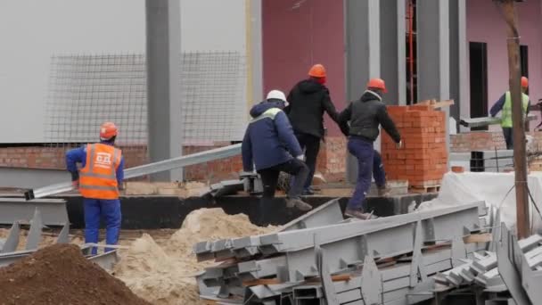 Un grupo de trabajadores masculinos con chaquetas y cascos amarillos está en el sitio de construcción . — Vídeos de Stock