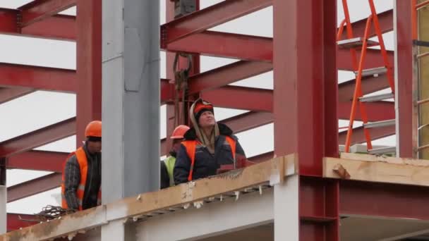 Eine Gruppe männlicher Arbeiter in gelben Jacken und harten Hüten arbeitet in luftiger Höhe mit Eisenträgern.. — Stockvideo