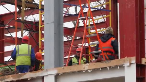 Sarı ceketli ve sert şapkalı bir grup erkek işçi demir kirişli bir yükseklikte çalışıyorlar.. — Stok video