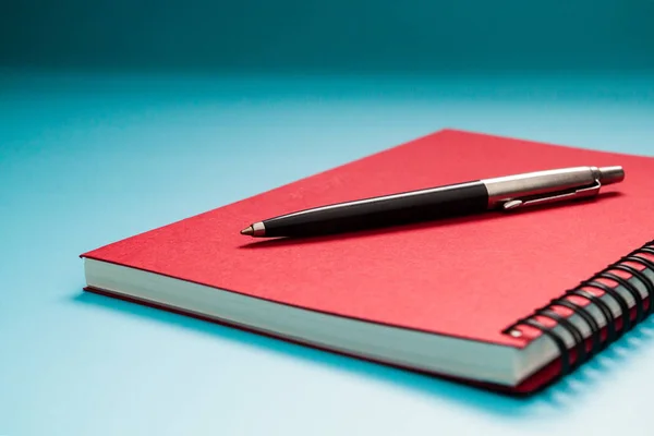 青いテーブルの背景に赤いノートブックとペン,学習のための概念 — ストック写真