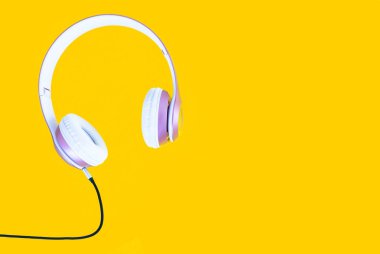 Pembe kulaklık ve siyah kablo pastel renk sarı arka plan üzerinde. Müzik konsepti. Boş kopya alanı