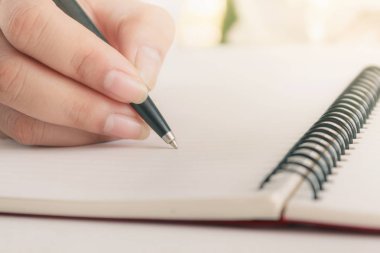 Defter üzerinde kalem yazısı olan kadın el. Boş kopya alanı.