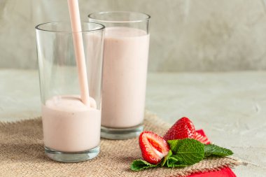 Uzun bardakta milkshake, çilek, nane, çuval bezi rahat bir atmosfer yaratır, bardağa kokteyl döker.