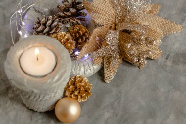  Gümüş sarısı tonlarda güzel bir Noel dekoru, alışılmadık bir çiçek, kozalaklar ve yanan bir mum, şık ve modern.