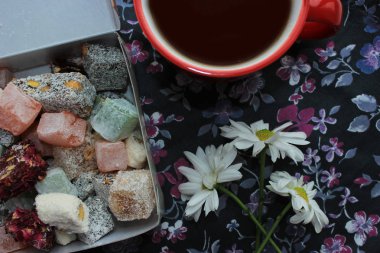 Kahvaltı kavramı kırmızı bir fincan, Türk lokumu ve koyu arka plan üzerinde taze papatya sıcak çay ile