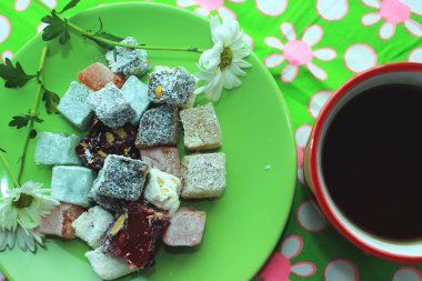 Kahvaltı kavramı kırmızı bir fincan, Türk lokumu ve yeşil zemin üzerine taze papatya sıcak çay ile