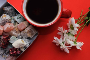 Kahvaltı kavramı kırmızı bir fincan, Türk lokumu ve kırmızı zemin üzerine taze papatya sıcak çay ile