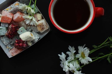 Kahvaltı kavramı kırmızı bir fincan, Türk lokumu ve siyah arka plan üzerine taze papatya sıcak çay ile