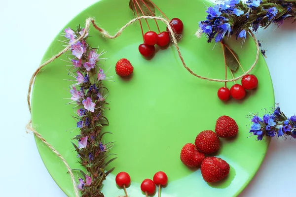 Summer season concept. Cherry, strawberry, flowers on green plate. Copy space