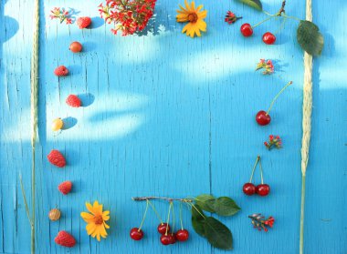 Olgun taze Bektaşi üzümü, ahududu ve kiraz kırmızı çiçekli bir ahşap masa turkuaz yakın çekim. Üstten yatay görünüm. 