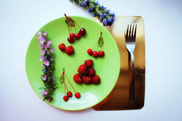 Summer season concept. Cherry and strawberry on green plate. Copy space