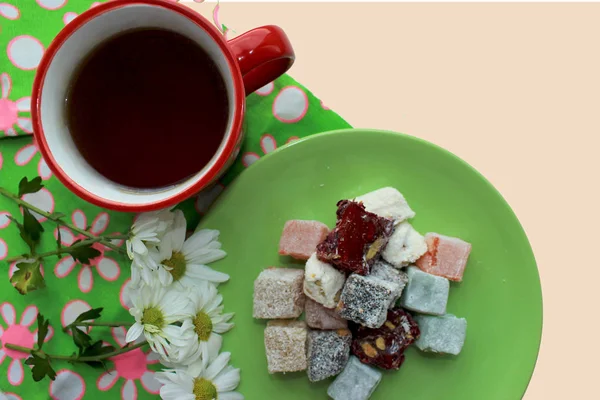 Kırmızı bir fincan, Türk lokumu ve yeşil zemin üzerine taze papatya sıcak çay ile Servis Kahvaltı. Üstten görünüm, kopya alanı