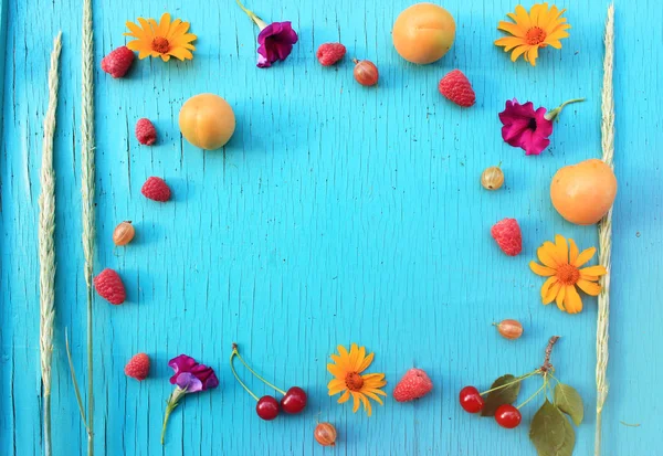 Besin zengin meyve. Olgun taze kayısı, Bektaşi üzümü ve ahududu ahşap masa turkuaz yakın çekim ve parlak çiçekler yaz. Üstten yatay görünüm. Metin için yer kopyalayın