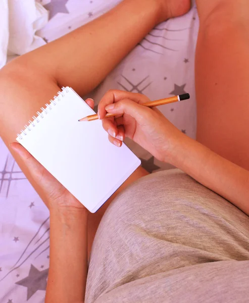 Pregnant woman makes a notes, plans with a notepad and pencil