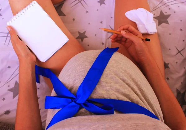 Pregnant woman makes a notes, plans with a notepad and pencil