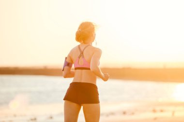 kulaklıklar içinde sporcumuz smartphone içinde çalışan güneş ışığına karşı sahilde koşu çantası ile dikiz 