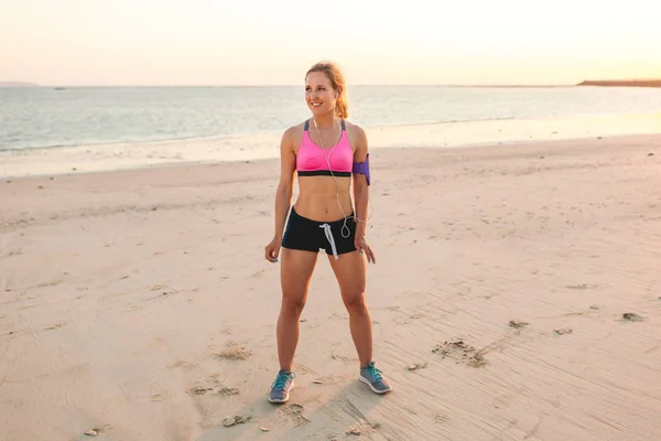 Glimlachend Sportvrouw Oortelefoons Met Smartphone Zaak Staande Armband Aan Zandstrand — Stockfoto