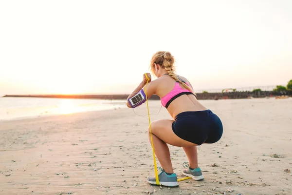Sportswoman Earphones Smartphone Armband Case Doing Exercise Stretching Band Beach — Stock Photo, Image