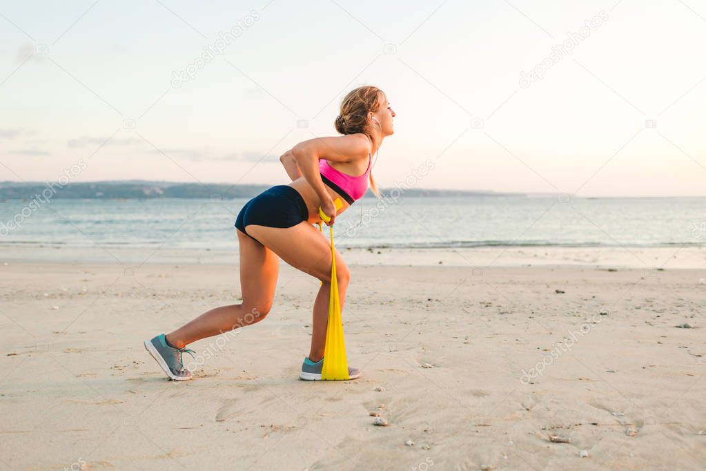 side view of sportswoman doing exercise with stretching band on beach 