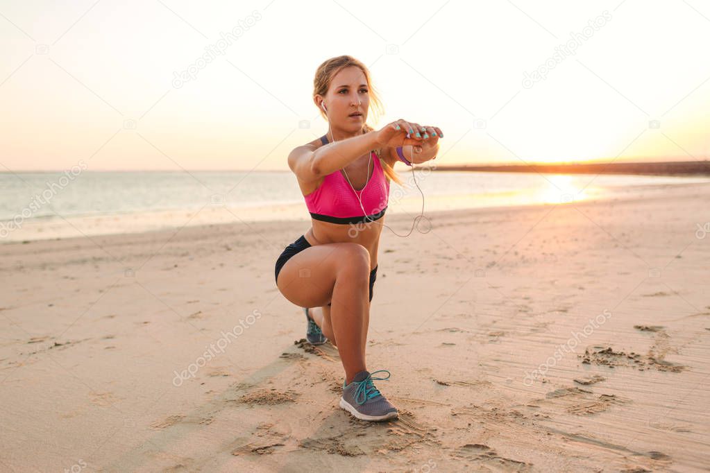 young sportswoman in earphones with smartphone in armband case doing exercise on beach 